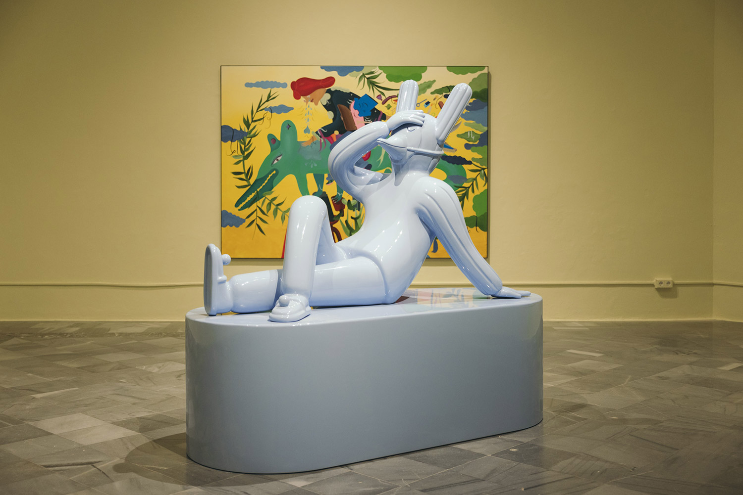 A massive baby blue, reclining sculpture by Hayon with a background of one of his paintings